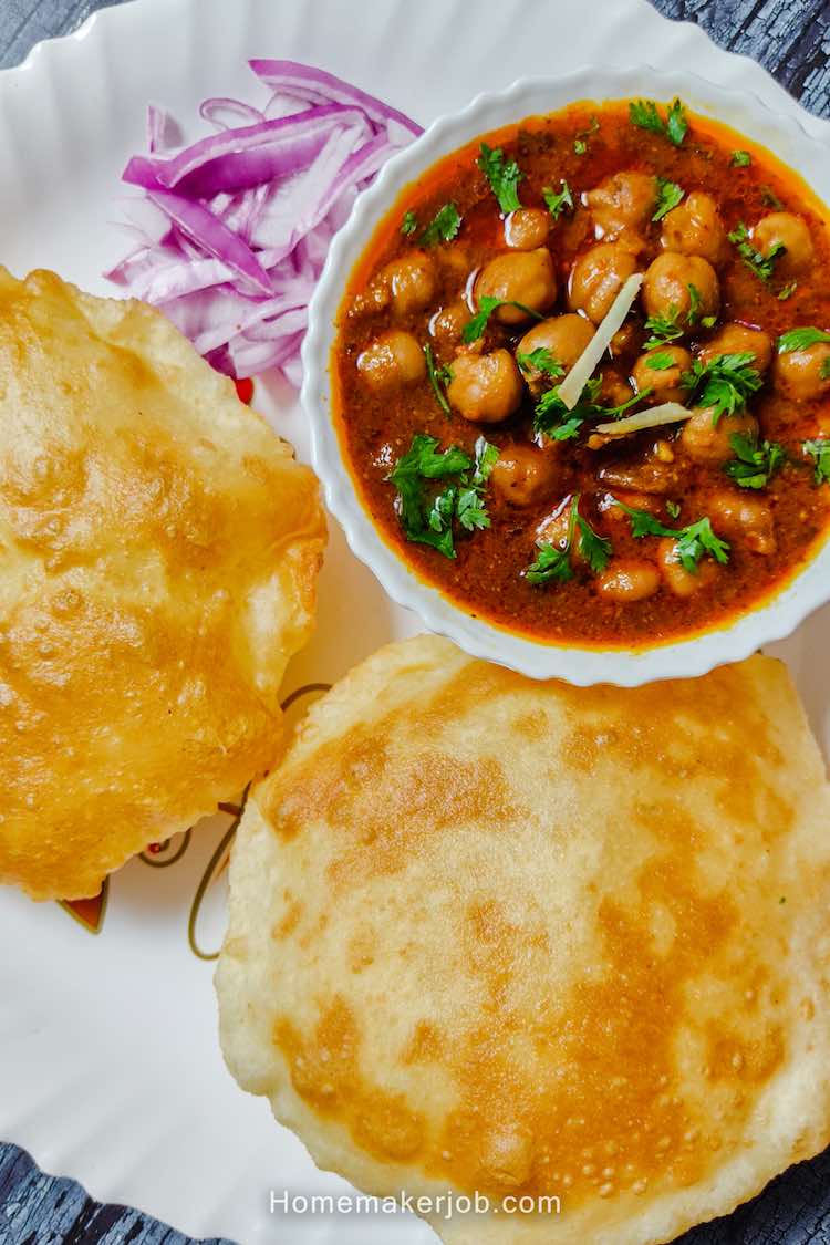 Top view of chhola in a white bowl, two bhaturas besides it, chopped onion in the corner for garnishing, a recipe by homemakerjob.com