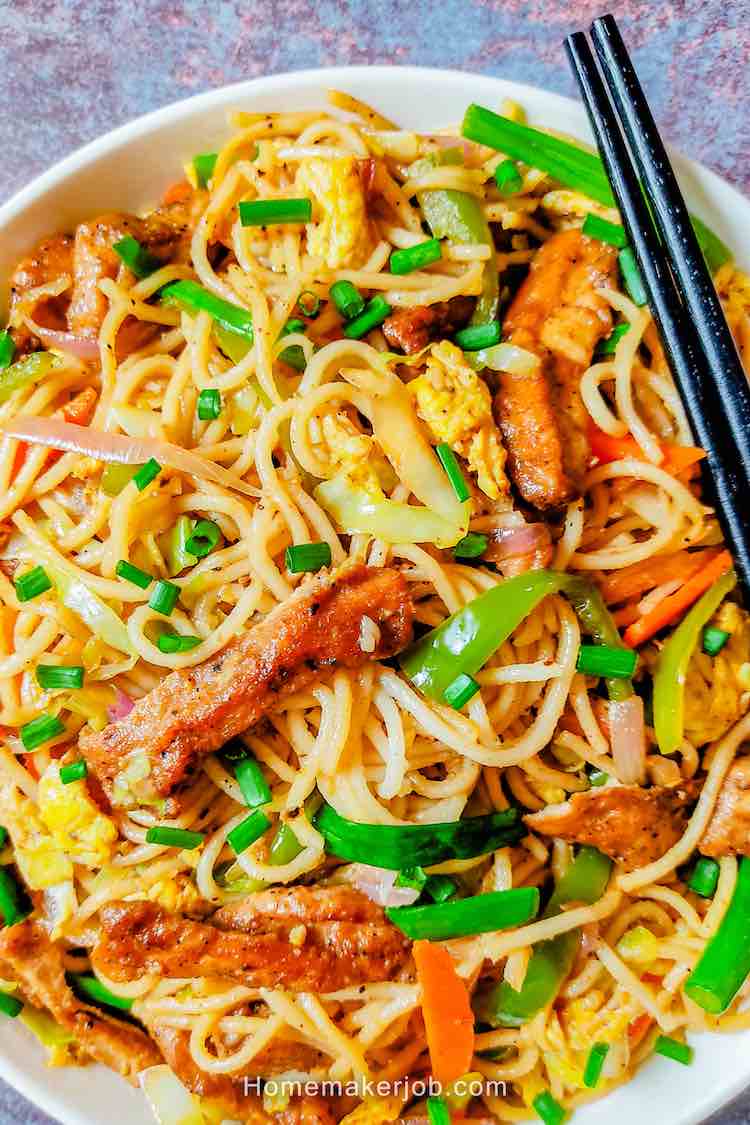 Tasty hot chicken Hakka Noodles by Homemakerjob, served in white dish with two black chopsticks kept on grey table top