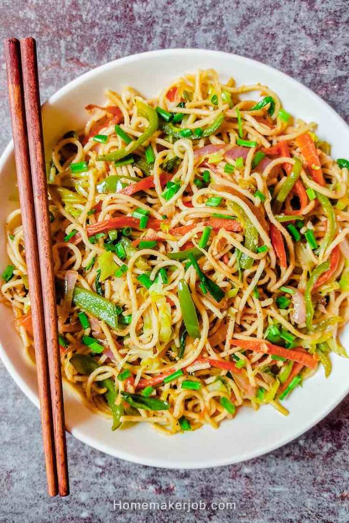 Main photo with top view of veg hakka noodles served in white dish along with red chopsticks, a recipe by homemakerjob