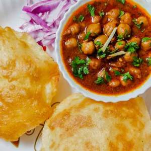 Top view of chhole in a white bowl, two bhature besides it, chopped onion in the corner for garnishing, a recipe by homemakerjob.com