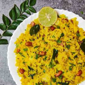 Top view photo of aloo kanda pohe served in a white plate garnished with curry leaves and lemon, a recipe by homemakerjob.com