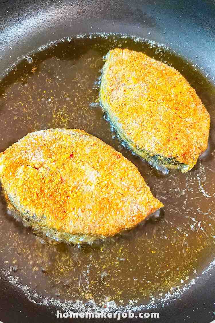 Two pieces of marinated surmai being shallow fried in frying pan or tawa