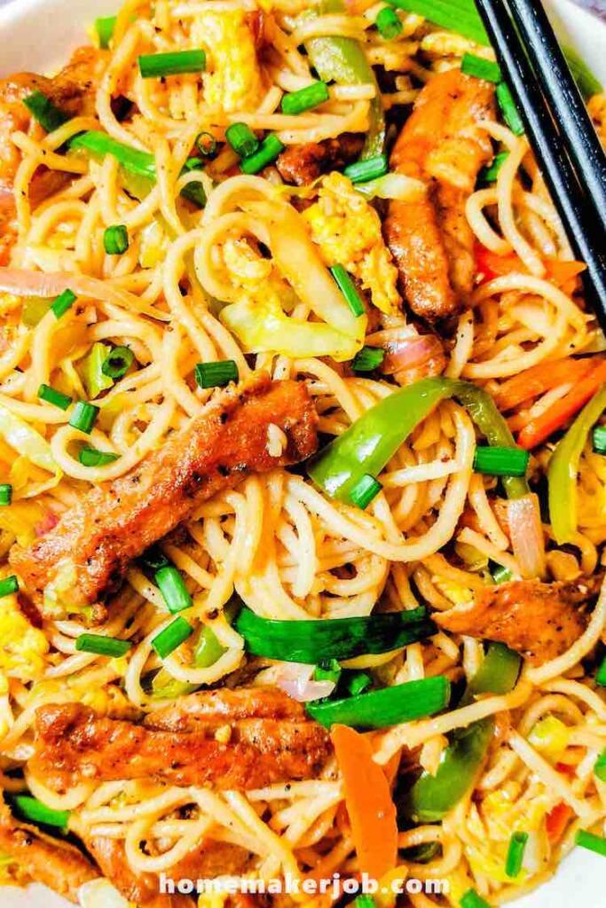 Chicken Hakka Noodles served hot in a white dish with two black chopsticks