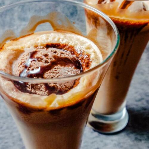 Two tall glasses filled with chilled chocolate milkshake and ice-cream on top