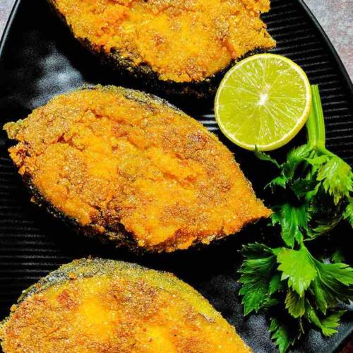 Three pieces of Surmai fry served hot with lime and curry leaves in a black dish by Homemakerjob.com