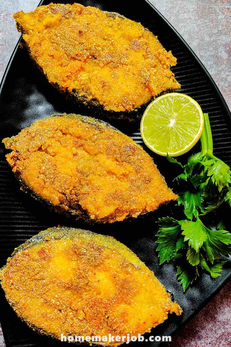 Three pieces of Surmai fry served hot with lime and curry leaves in a black dish by Homemakerjob.com