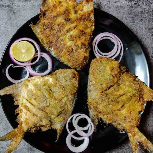 Three ready pieces of stuffed pomfret green masala fry served in a bliack dish garnished with onions and lemon wedges by homemakerjob