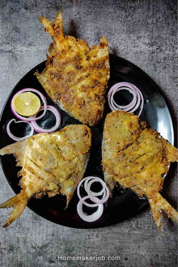 Three ready pieces of stuffed pomfret green masala fry served in a bliack dish garnished with onions and lemon wedges by homemakerjob
