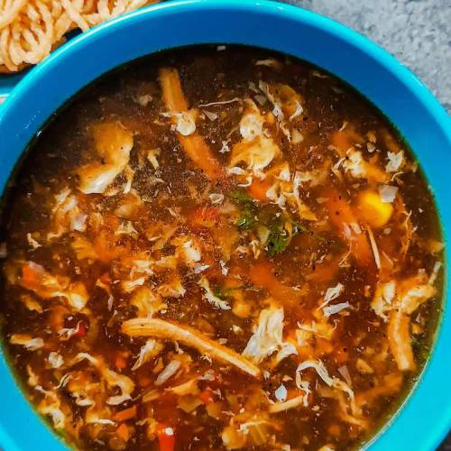 Close up photo of hot chicken manchow soup served in a blue bowl accompanied with dry fried noodles in a blue bowl on a table top, by homemakerjob.com