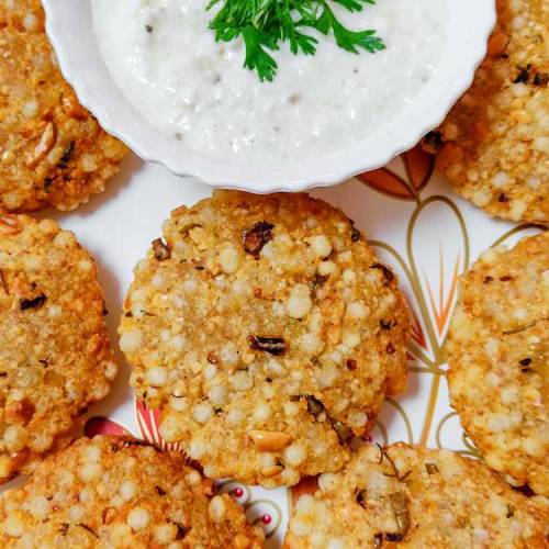 Close up photo of ready sabudana vada (sago pearls patty) served hot in a white dish with white curd chutney garnished with coriander leaves, by homemakerjob.com