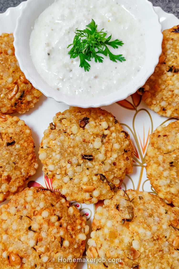 Close up photo of ready sabudana vada (sago pearls patty) served hot in a white dish with white curd chutney garnished with coriander leaves, by homemakerjob.com