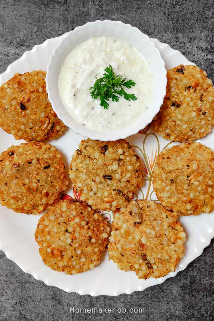 Photo of ready sabudana vada (sago pearls patty) served hot in a white dish with white curd chutney garnished with coriander leaves, by homemakerjob.com