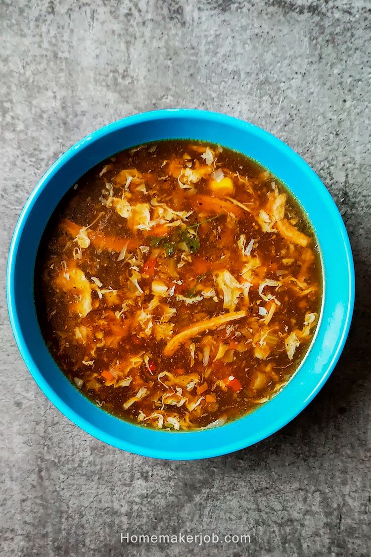 Chicken manchow soup served hot in a blue bowl on table top, by homemakerjob.com