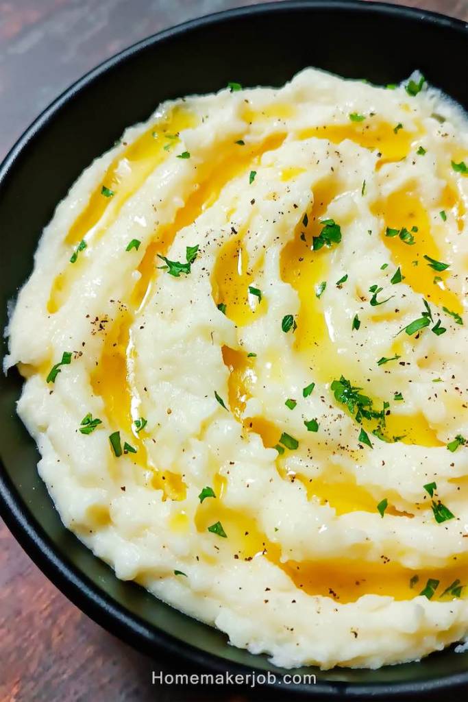 Close up photo of ready creamy butter garlic mashed potatoes served hot in a black dish on a table by homemakerjob