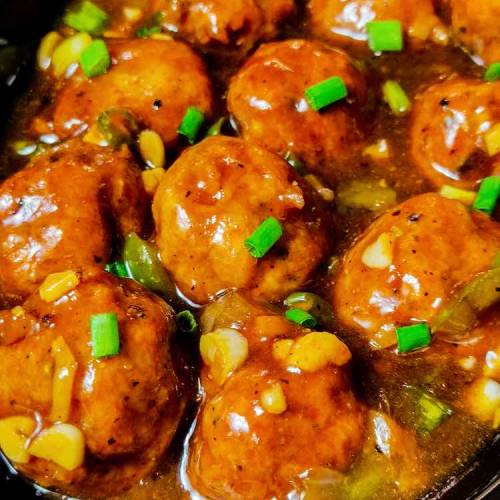 Close up photo of ready restaurant style chicken manchurian gravy served in a black plate on a table, by homemakerjob.com