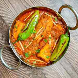 Achari chicken masala served with green bhavnagari chilies in a small kadai pot on a table top by homemakerjob.com