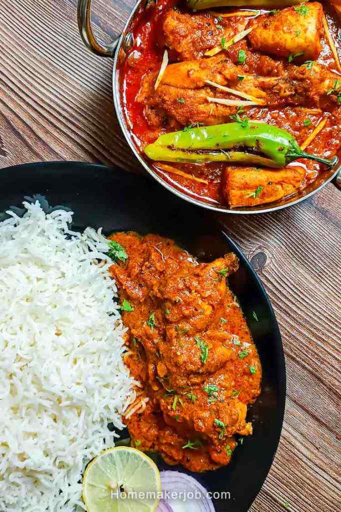 Ready hot chicken achari masala served with rice in a black plate along side a kadai pot containing remaining curry, on table top by homemakerjob.com