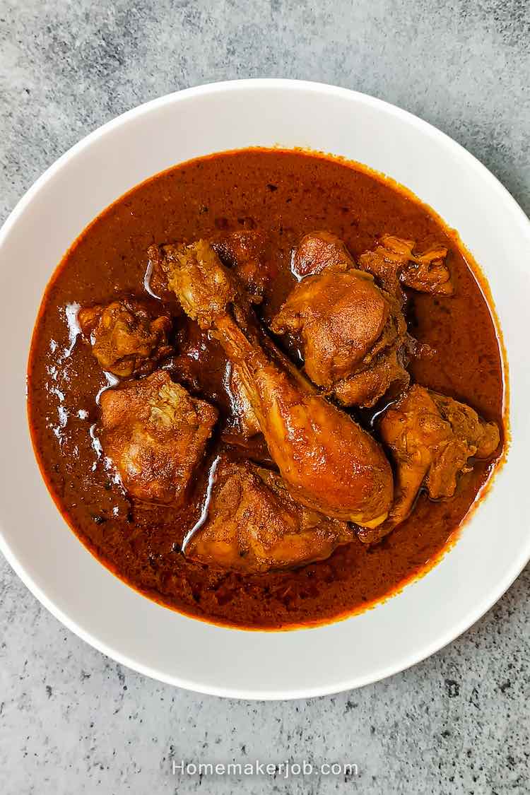 Spicy chicken kolhapuri with big chicken pieces in it served hot in a white bowl on a table top by homemakerjob.com