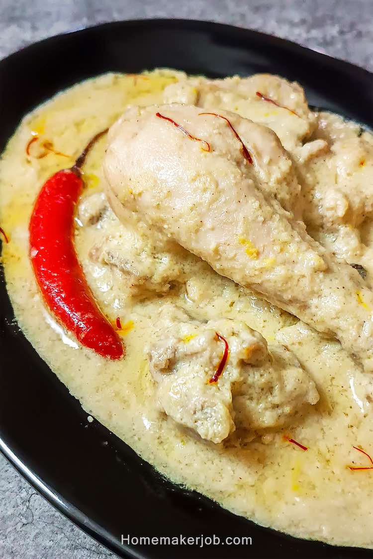 Close up photo shot of chicken rezala curry garnished with red chili, served hot in a black plate on table top, by homemakerjob.com