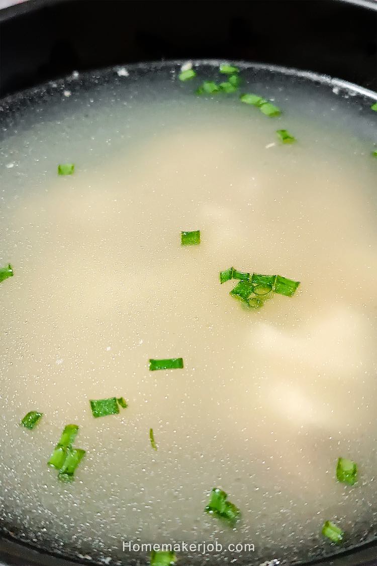 Close up photo of hot chinese chicken clear soup served in a black bowl, by homemakerjob