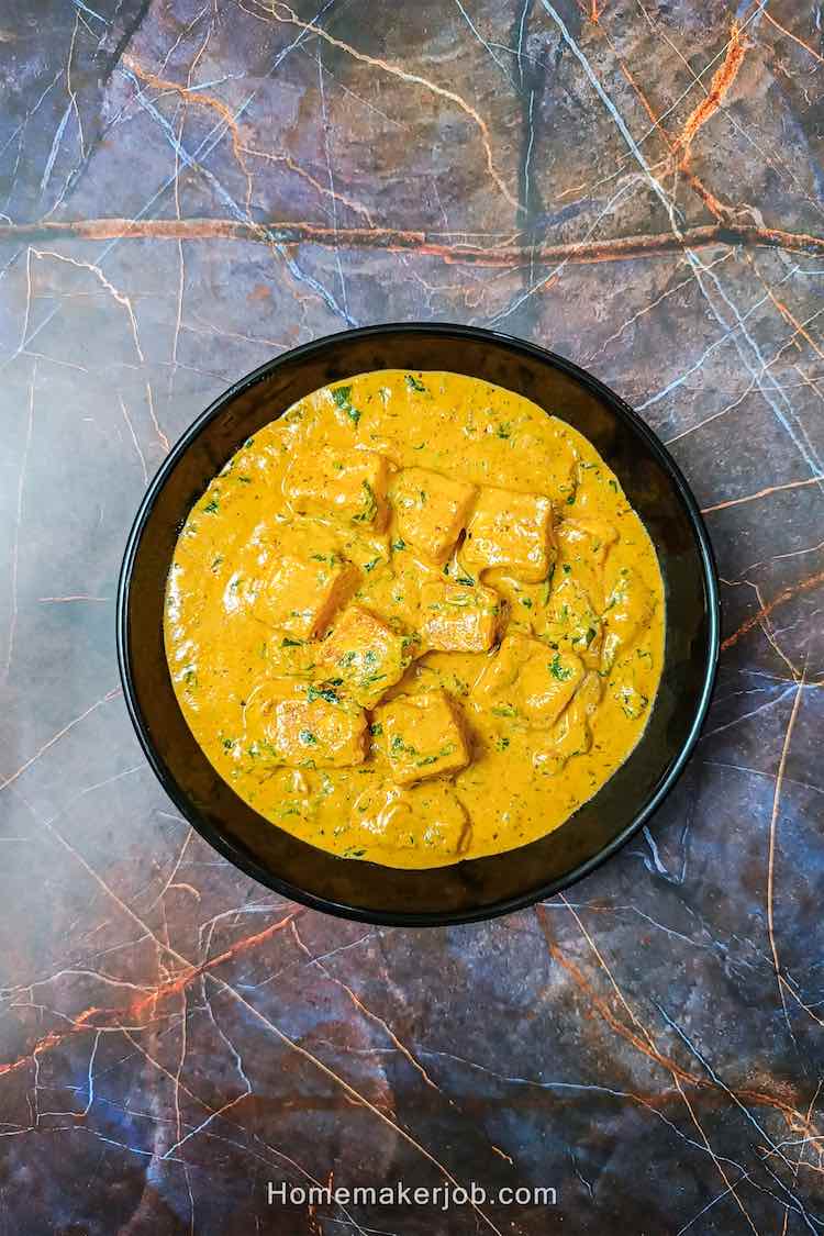 Top view photo of ready methi malai paneer served in a black bowl on a table, by homemakerjob.com