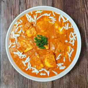 Paneer lababdar served hot in a white dish on a table, garnished with chopped coriander in the middle and grated cottage cheese around the edges, a recipe by homemakerjob