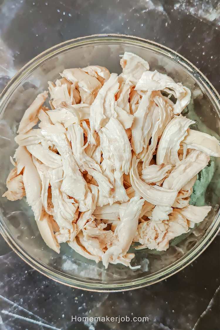 Top view photo of boiled chicken strips in a big glass bowl, as an ingredient for bharta chicken recipe by homemakerjob.com