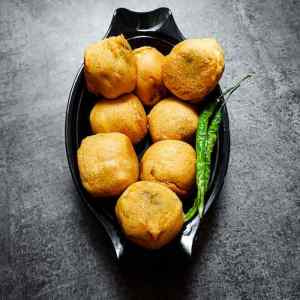 Photo of ready batata vada garnished with green chilies and served hot in a black dish on a table, by homemakerjob