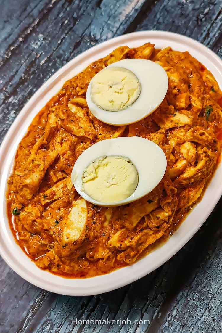 Chicken bharta served hot and garnished with two halves of cut boiled egg, in a steel dish on a table by homemakerjob