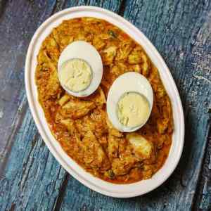 Chicken bharta served hot and garnished with two halves of cut boiled egg, in a steel dish on a table by homemakerjob