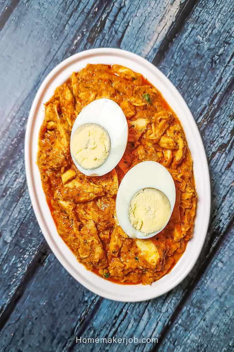 Chicken bharta served hot and garnished with two halves of cut boiled egg, in a steel dish on a table by homemakerjob