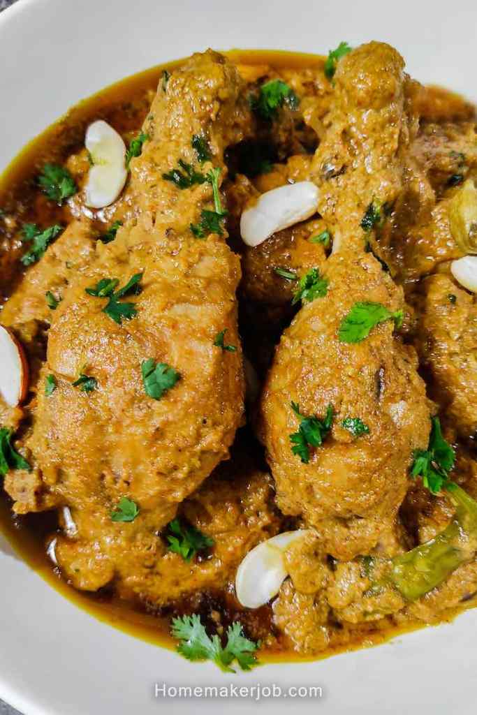 Close up of mughlai chicken garnished with cashews and chopped coriander leaves on top, served hot in a white bowl, a recipe by homemakerjob