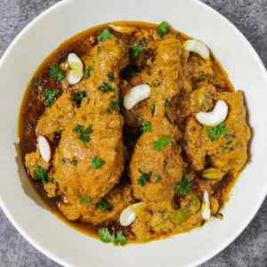 Chicken mughlai garnished with cashews and chopped coriander leaves on top, served hot in a white bowl, a recipe by homemakerjob