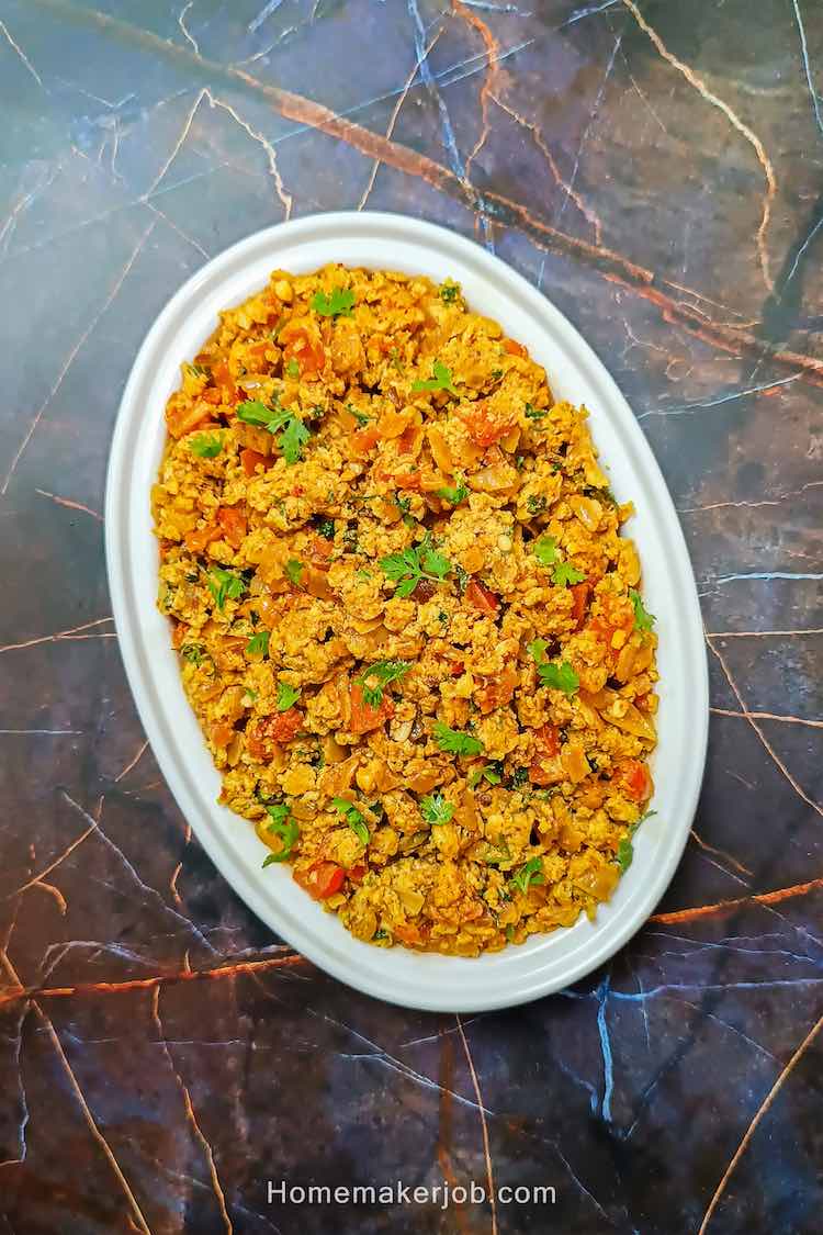Egg bhurji served hot in a oval shaped white dish on a table top by homemakerjob.com