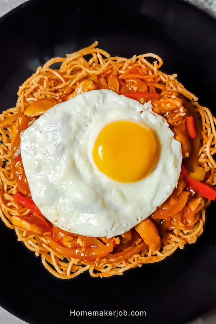 Hot indo-chinese chicken chop suey with dry noodles, garnished with half fry egg, served in a black plate by homemakerjob.com