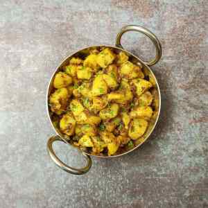 Photo of tasty jeera aloo in a small steel kadai on a table top, a recipe by homemakerjob.com