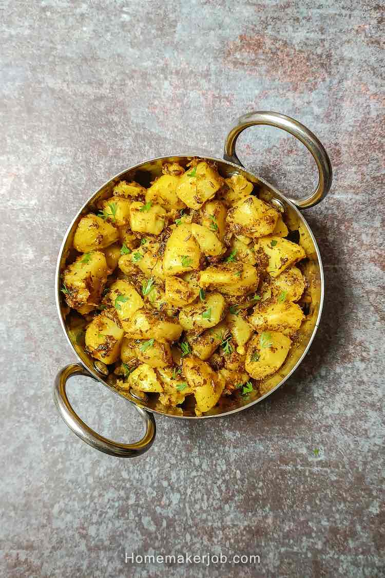 Photo of tasty jeera aloo in a small steel kadai on a table top, a recipe by homemakerjob.com