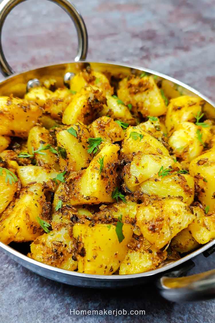 Tilted angle close up photo of tasty jeera aloo in a small steel kadai on a table top, a recipe by homemakerjob.com