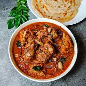 ready malabar chicken curry served hot in a white dish, with paretta in another dish and curry leaves spread on table top for decorating, by homemakerjob