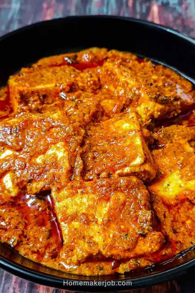 Close up photo of achari paneer masala in a black bowl on a table top, a recipe by homemakerjob