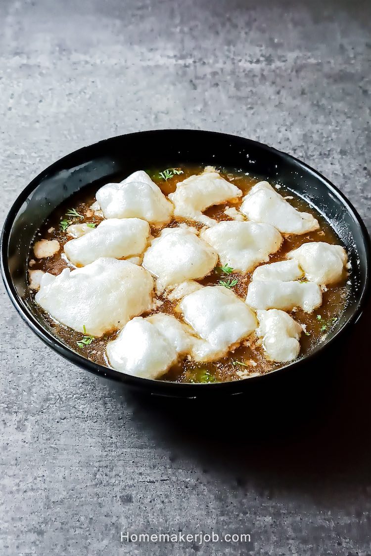 Top view photo of chinese chicken long fong soup served hot in a black bowl on a table, while egg white icebergs floating on the top of soup; a recipe by homemakerjob.com