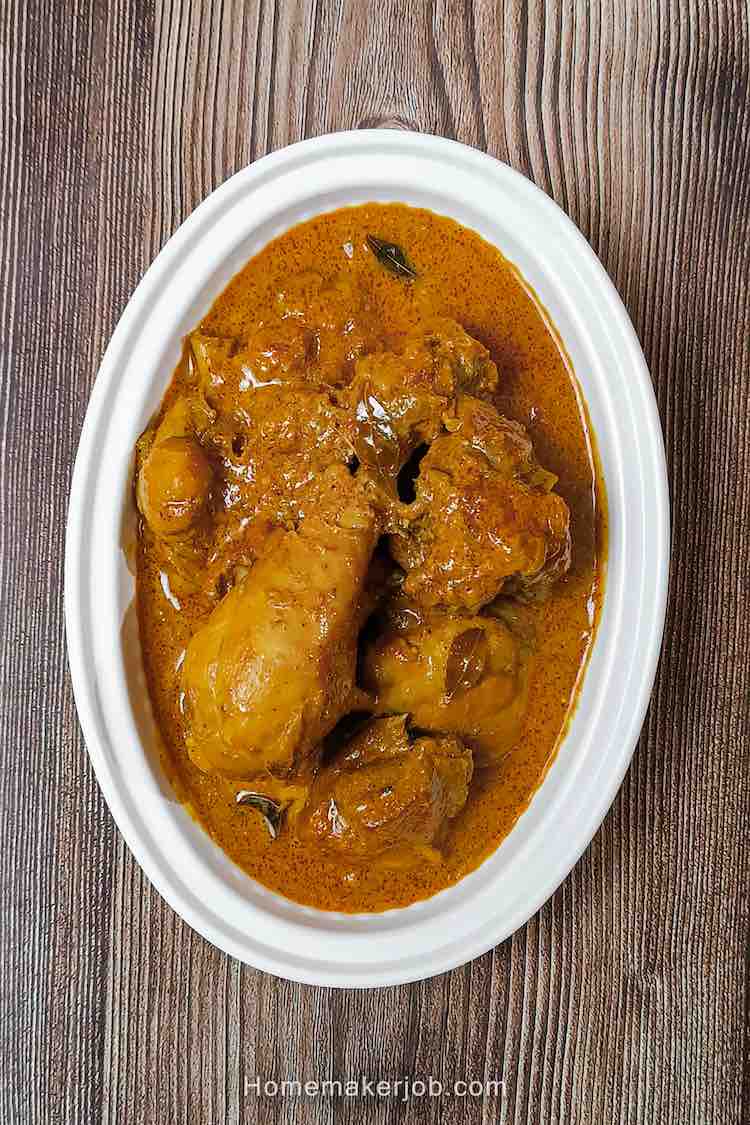 Top view photo of madras chicken curry Indian style, served hot in a white oval shaped bowl, on a table, a recipe by homemakerjob.com