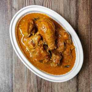 Top view photo of madras chicken curry Indian style, served hot in a white oval shaped bowl, on a table, a recipe by homemakerjob.com