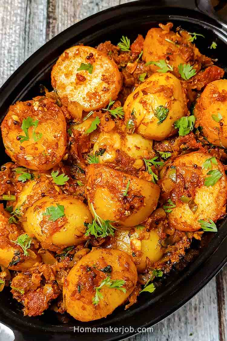 Top view close-up photo of Bombay potatoes (aloo) served hot in a black oval shaped bowl, on a table, a simple traditional recipe by homemakerjob.com