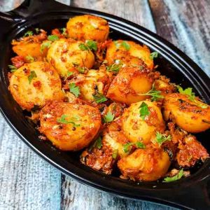 Photo of bombay potatoes (aloo) served hot in a black oval shaped bowl, on a table, an easy recipe by homemakerjob.com