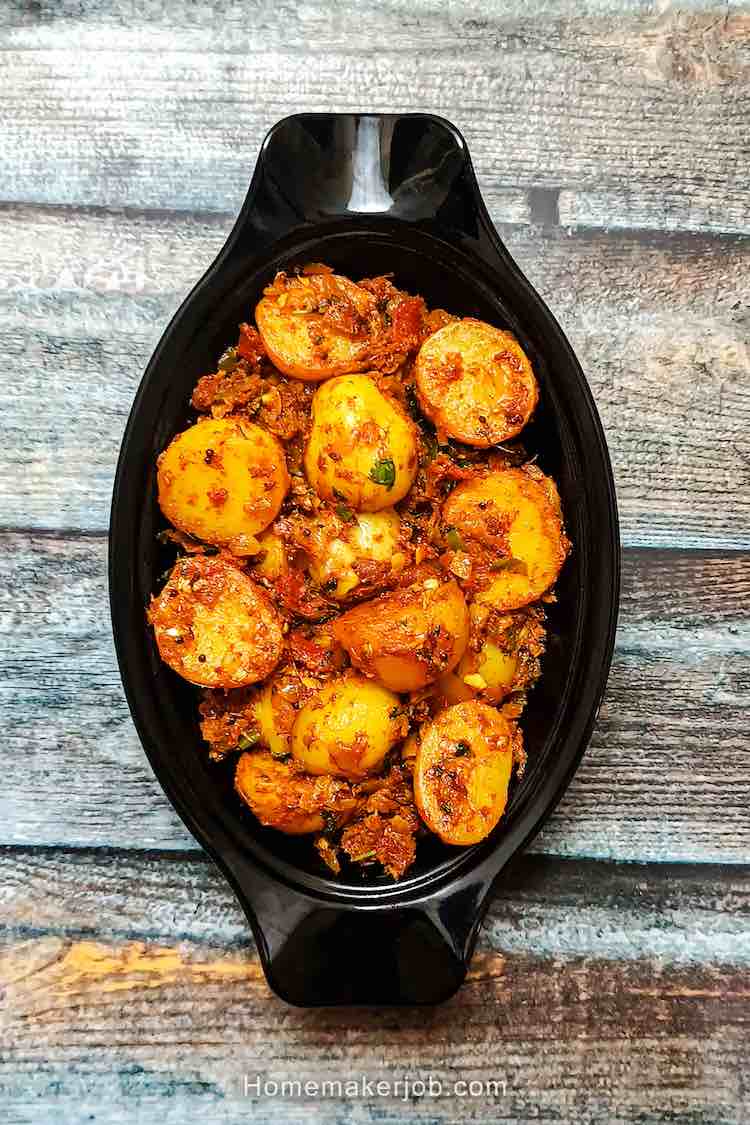 Top view photo of Bombay potatoes (aloo) served hot in a black oval shaped bowl, on a table, an authentic traditional recipe by homemakerjob.com