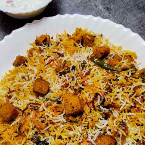 Soya bean chunks veg biryani served hot in a white plate with onion raita in a small bowl as a side dish, a recipe by homemakerjob.com