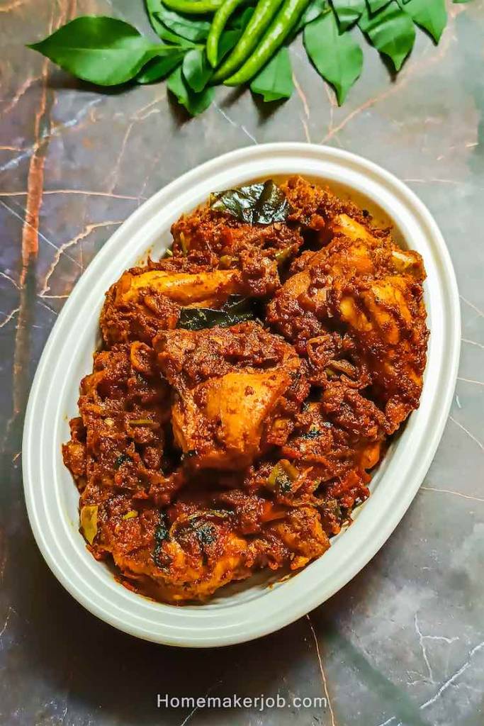 Chicken chukka dry masala gravy in a white bowl, decorated with curry leaves and green chilies beside the bowl on a table, a recipe by homemakerjob.com