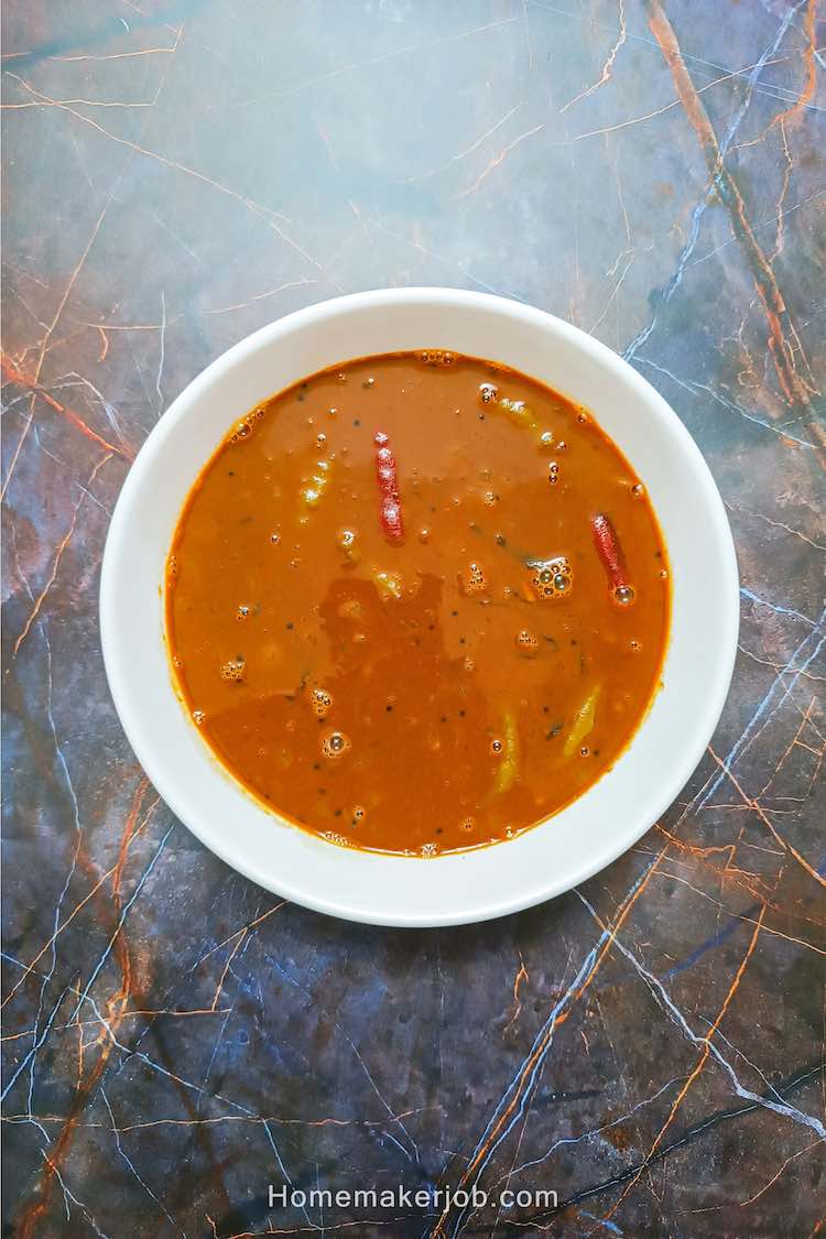 A top view photo of Ulava charu a.k.a. horse gram or kollu lentil rasam soup in a white bowl on a table top, a recipe by homemakerjob.com
