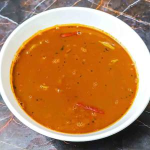 A top view photo of Ulava charu a.k.a. horse gram or kollu lentil rasam soup in a white bowl on a table top, a recipe by homemakerjob.com